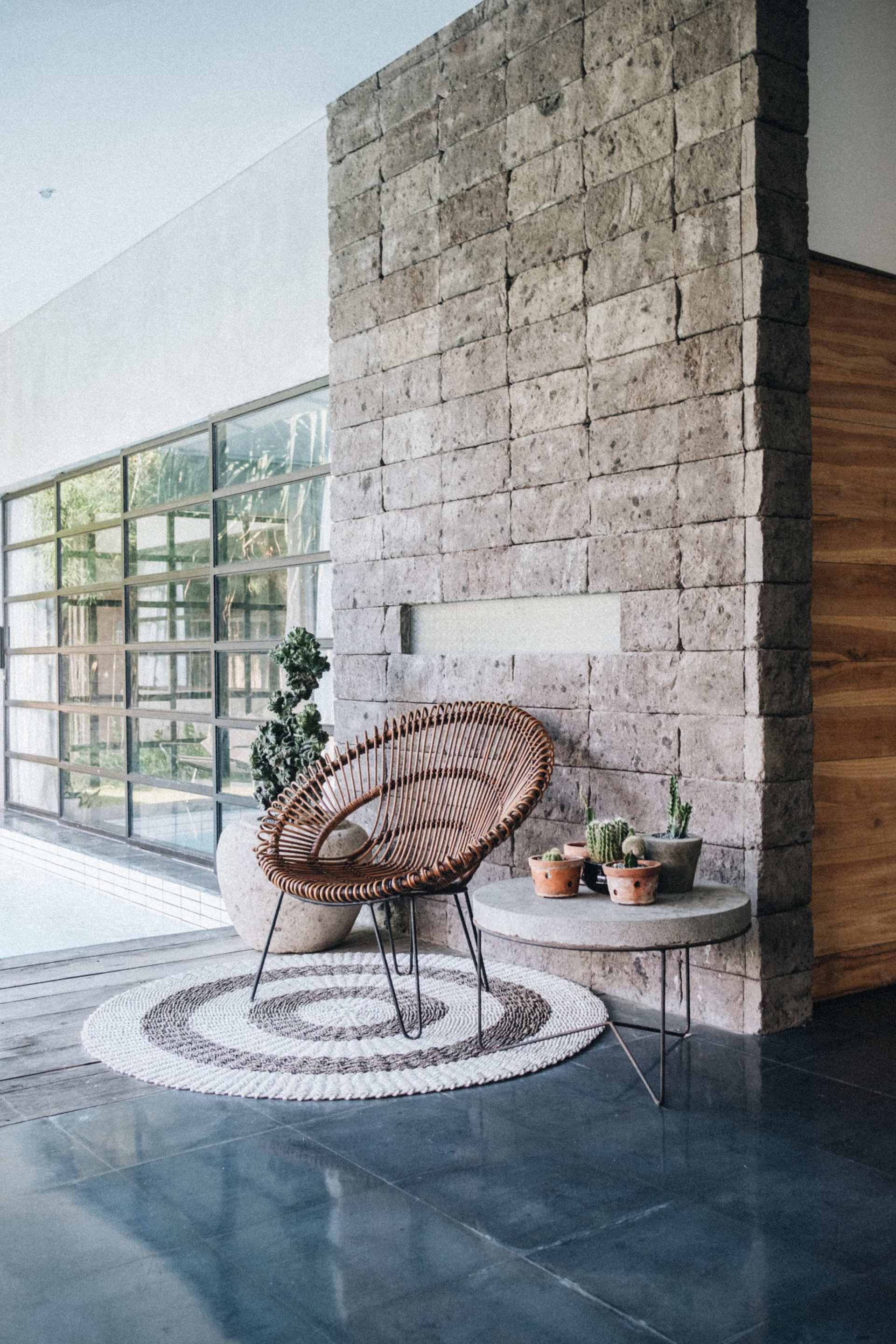 Modern interior with a woven lounge chair and potted plants beside a tall stone wall.