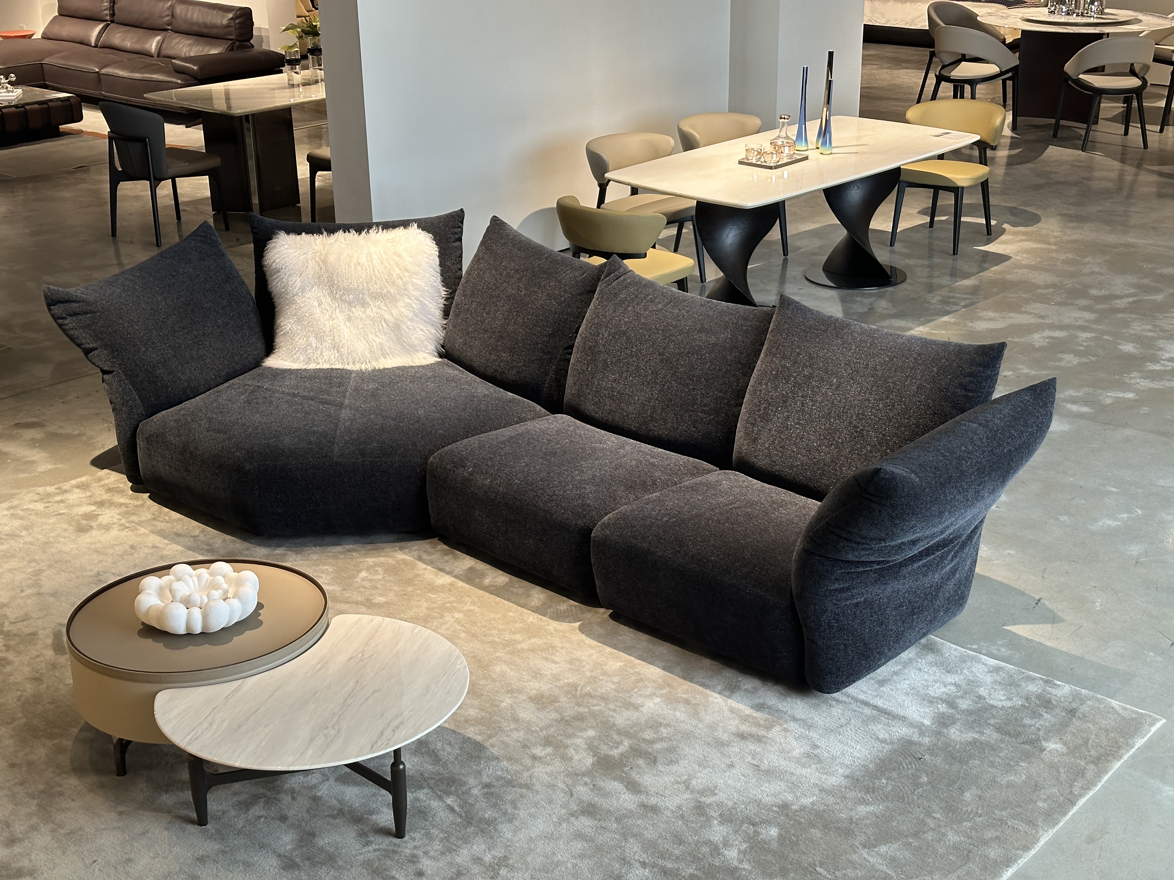 Three-quarter view of charcoal curved modular sofa with flared wing arm and white faux-fur accent pillow