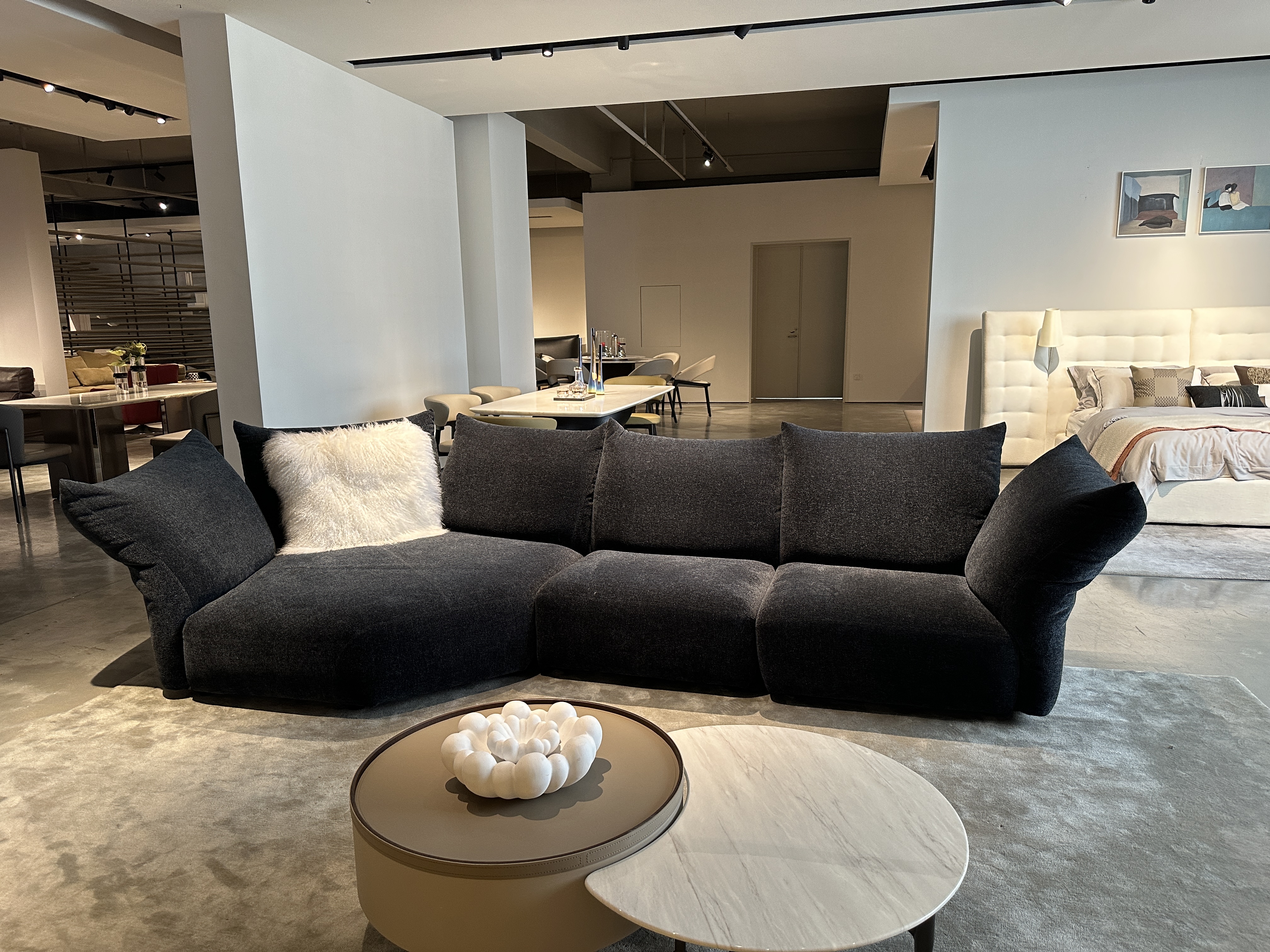 Wide showroom angle of charcoal flared-arm modular sofa with marble nesting tables and dining backdrop