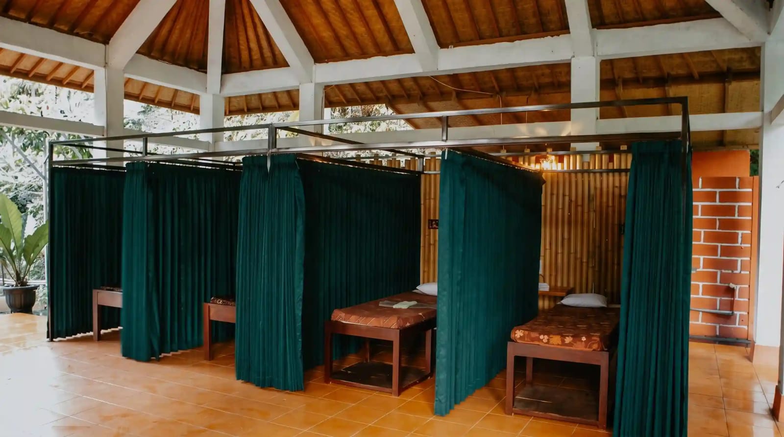 Traditional open-air Balinese massage pavilion with woven bamboo walls, crisp white linen treatment bed, frangipani blossoms, essential oils, and panoramic views of lush highland flora in Munduk