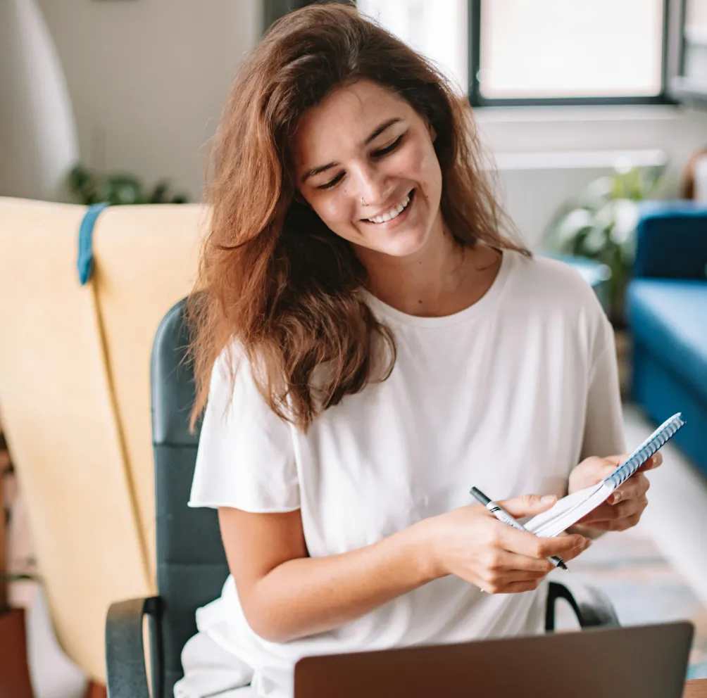 Woman holding notepad sitting at desk, taking notes as she attends a digital event.
