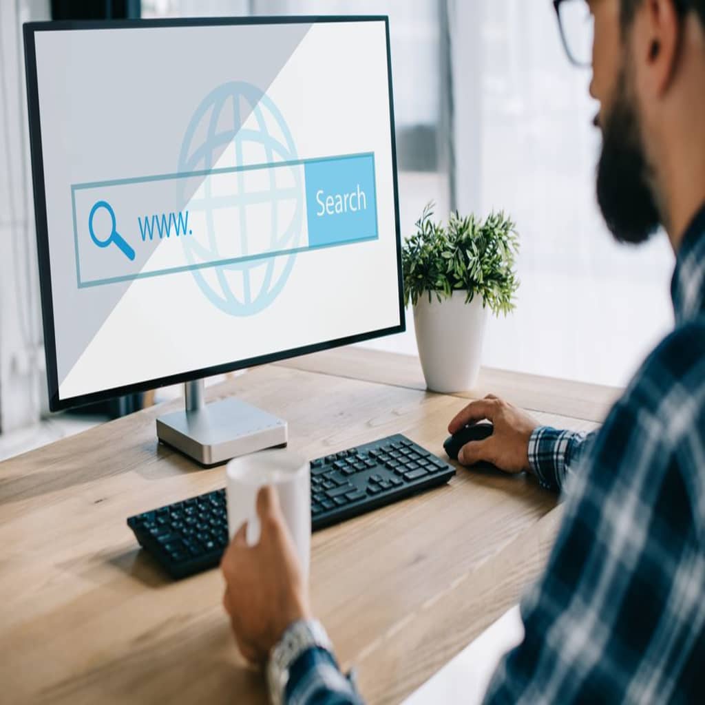 Man with a cup in hand clicking a mouse to make an ecommerce search.