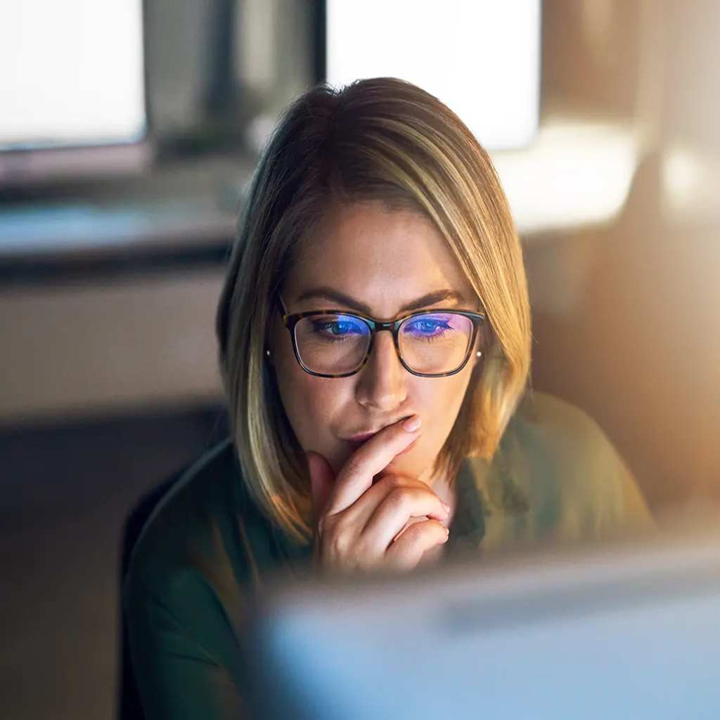 A woman with glasses looks at a computer monitor as she compares Bluehost alternatives for WordPress hosting