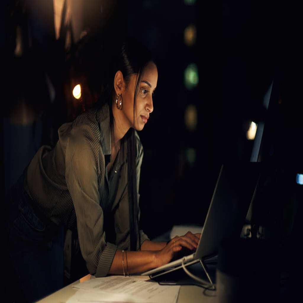 A young woman sits and gazes over her laptop computer as she researches managed WordPress hosting