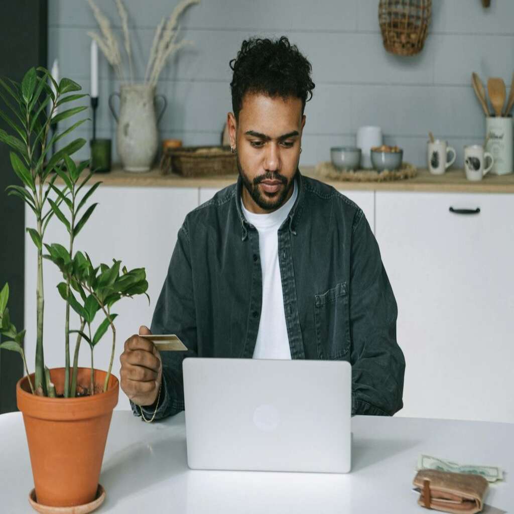 Man Holding a Card While Looking at the Screen of a Laptop