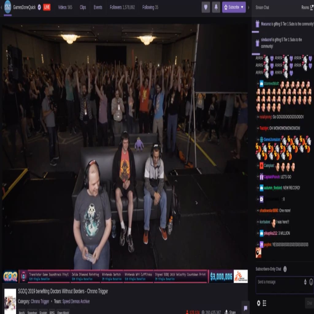 A screenshot of a gaming marathon shows a crowd of people watching behind gamers playing as well as a stream of online comments.