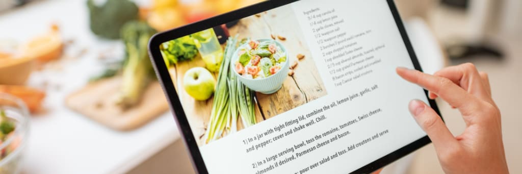 A recipe is displayed on a tablet while a person uses their finger to scroll the page.