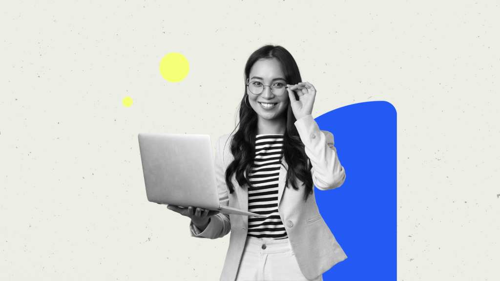 A woman with glasses holding a macbook pro with one hand while looking at the camera