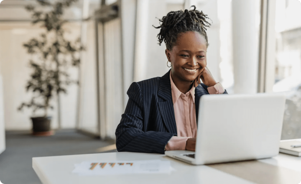 A woman in business attire on a conference call, she smiles at her laptop.