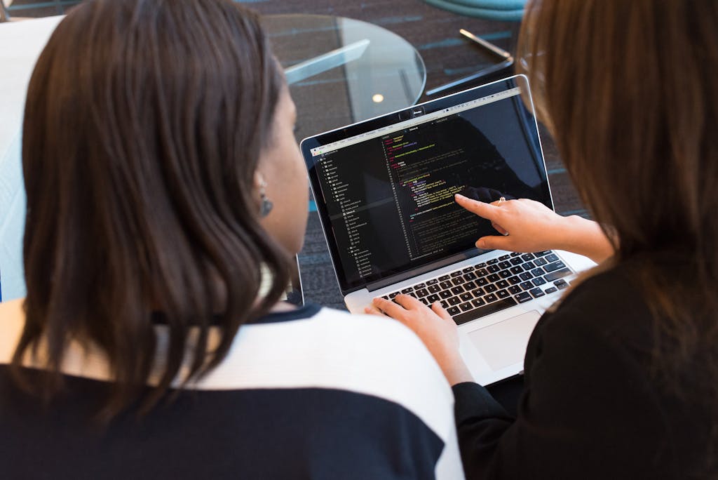Two women looking at application code on a laptop