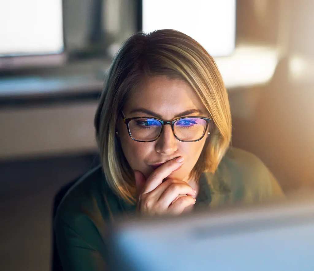 A woman with glasses looks at a computer monitor as she compares Bluehost alternatives for WordPress hosting