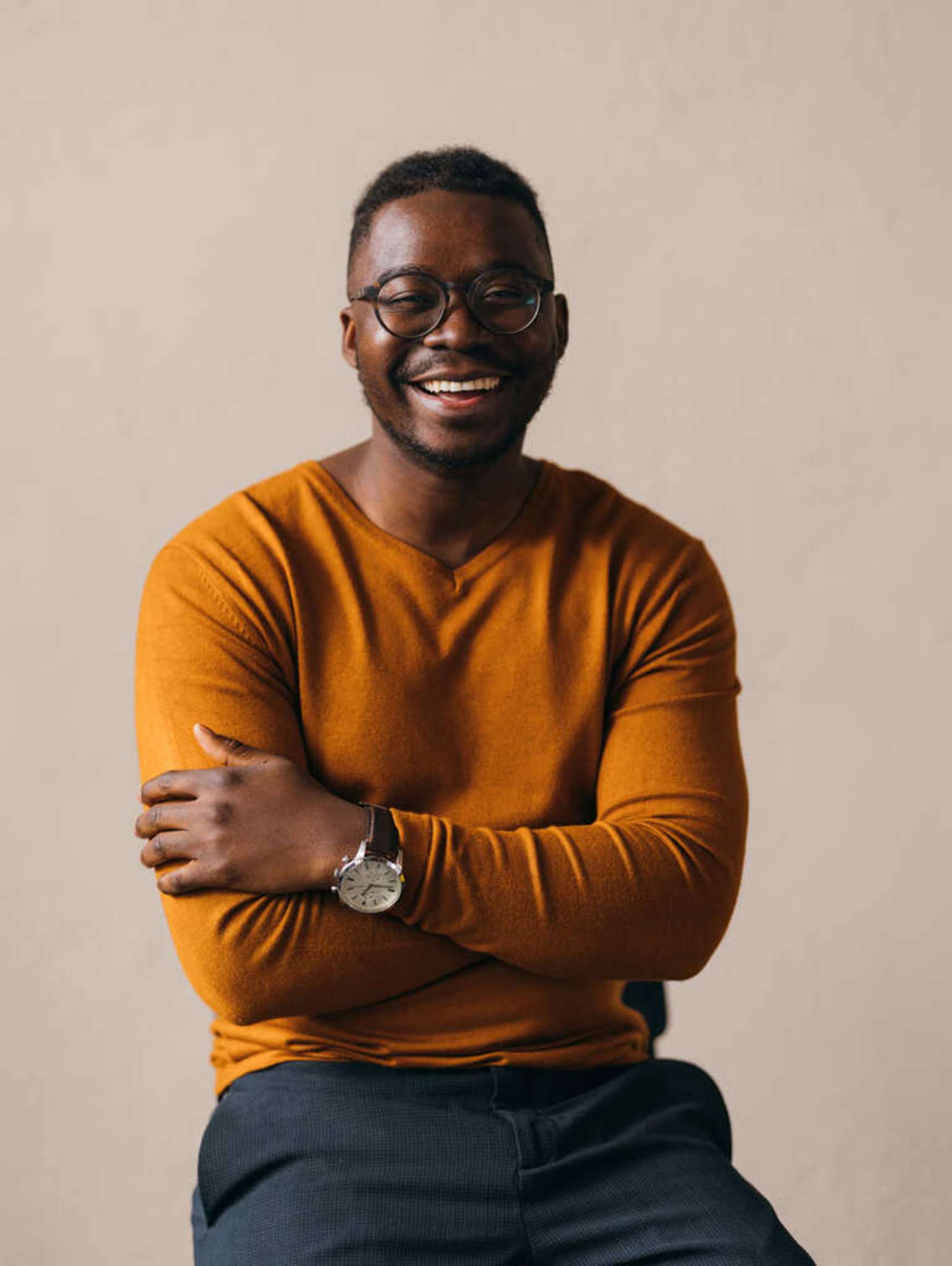 An agency partner with glasses sits on a stool with his arms crossed laughing