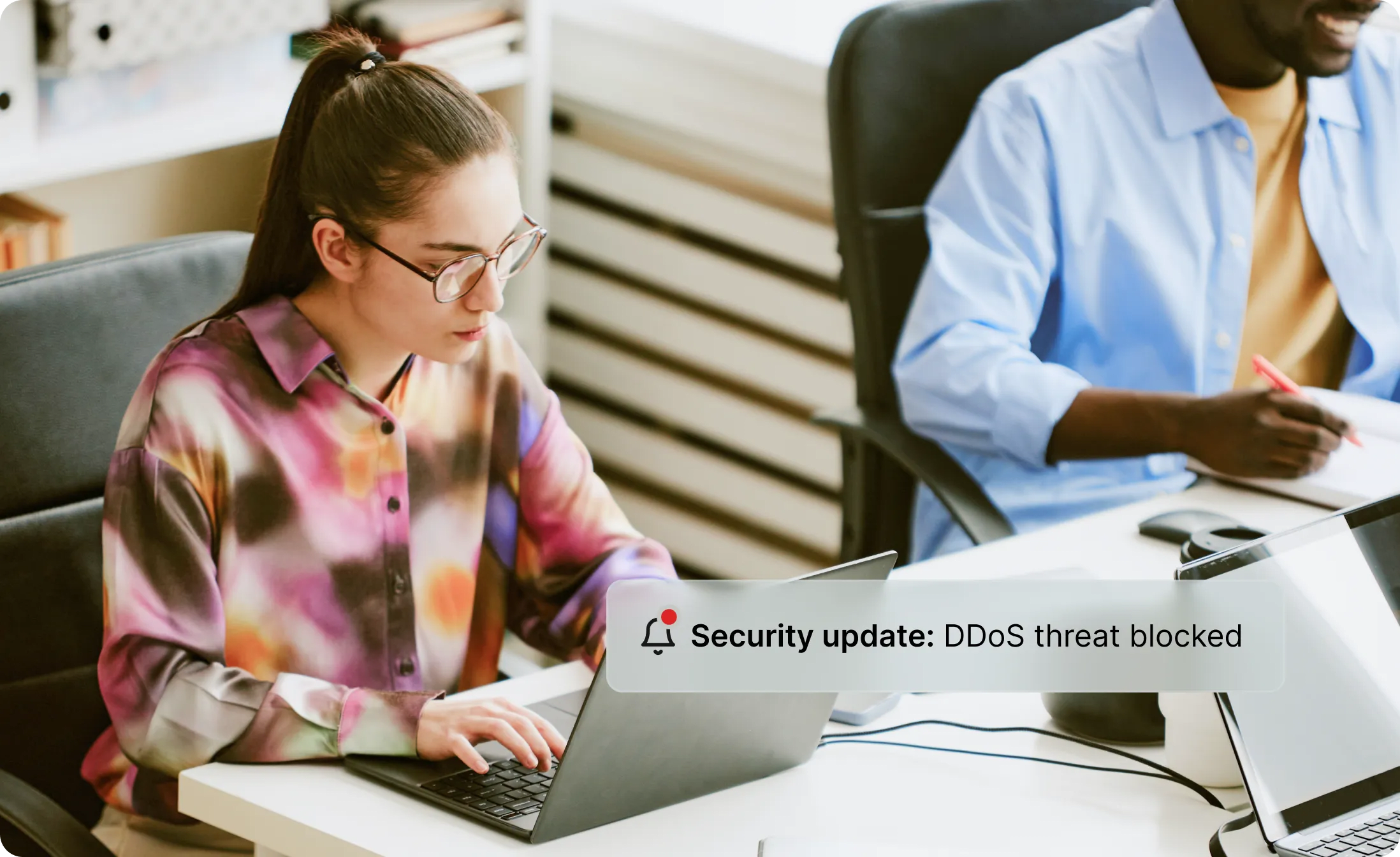 Woman typing on her laptop with an alert that says Security update: DDoS threat blocked.