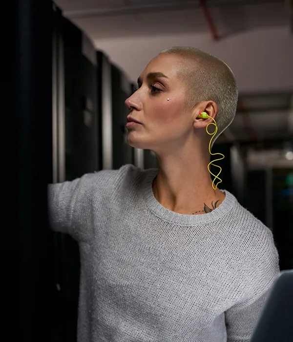 A woman in a loose cotton shirt listens to music on her earbuds as she checks bare metal servers in a data center