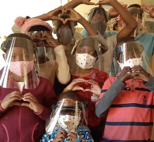 Children at Marang House wearing face masks and shields, making heart shapes with their hands