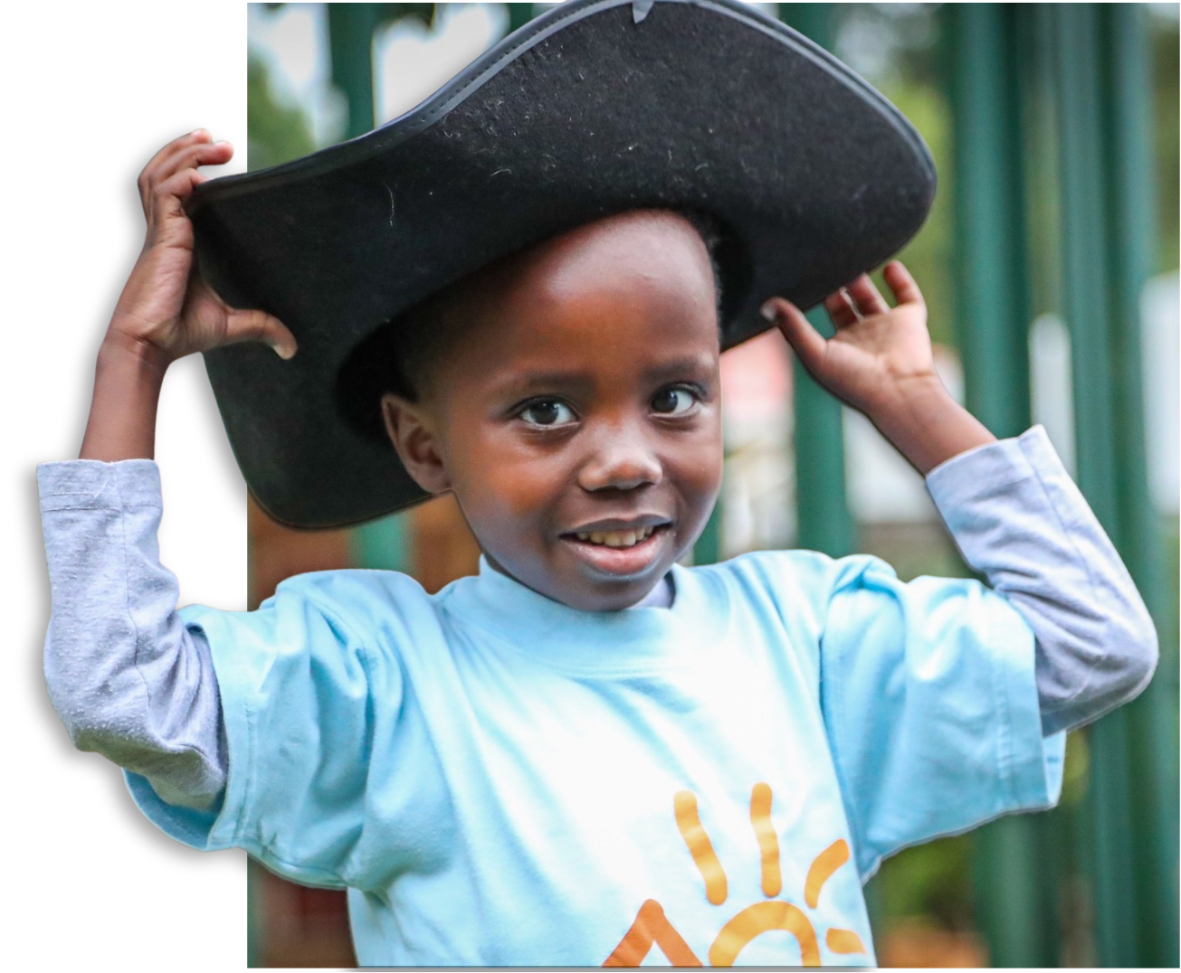A boy at Marang House smiling while holding up an oversized pirate hat