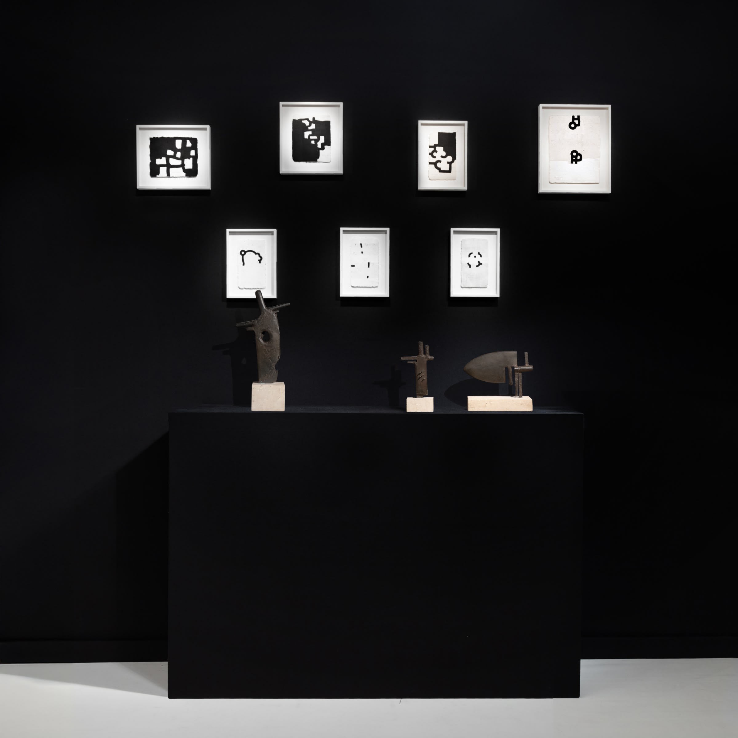 Installation view at Salon Art + Design 2024 in New York, with framed works arranged on a black wall above a pedestal with floor-standing works.