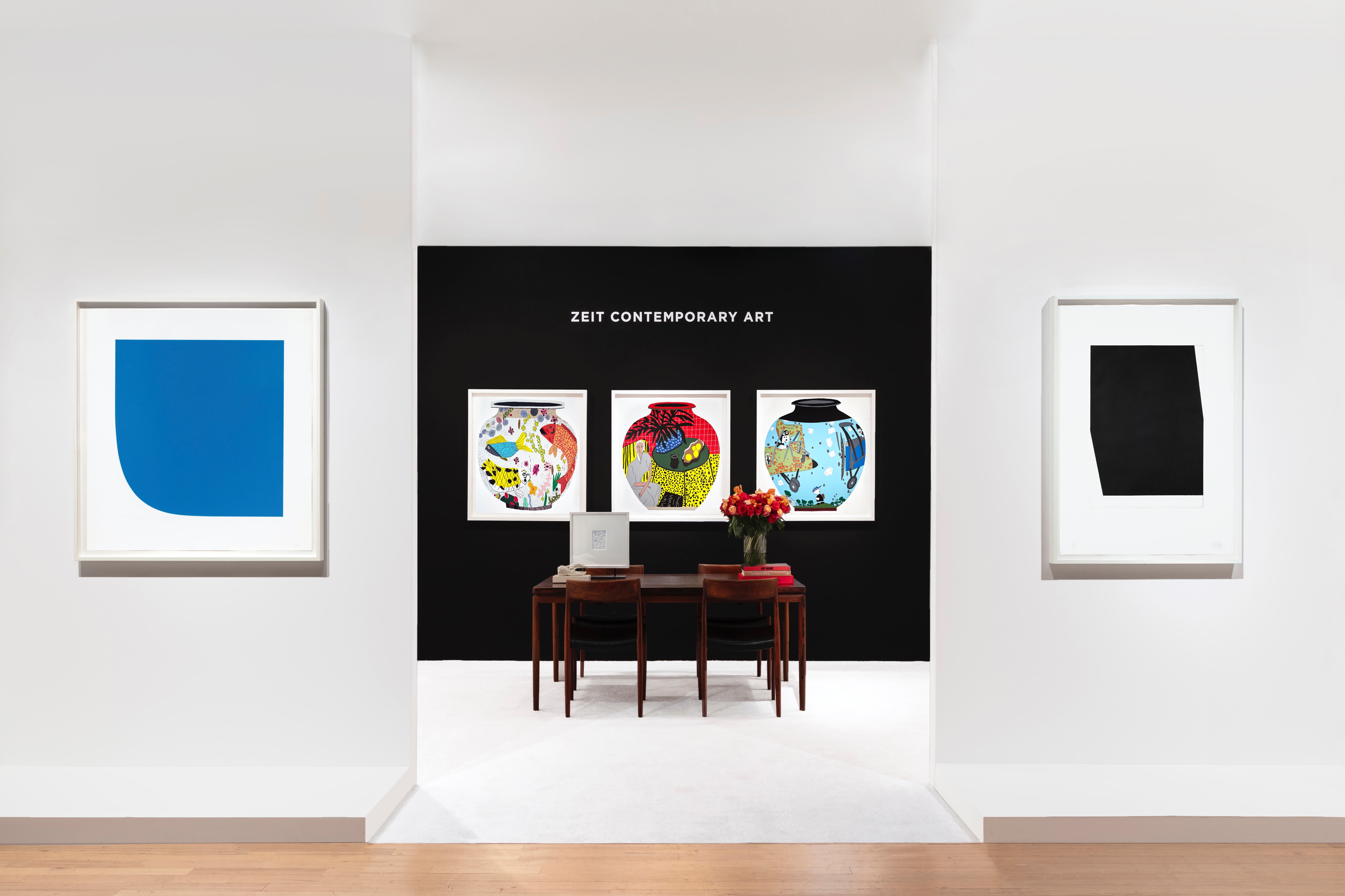 Installation view at Salon Art + Design 2023 in New York, with framed works across white booth walls and a central black accent wall above a table and chairs.
