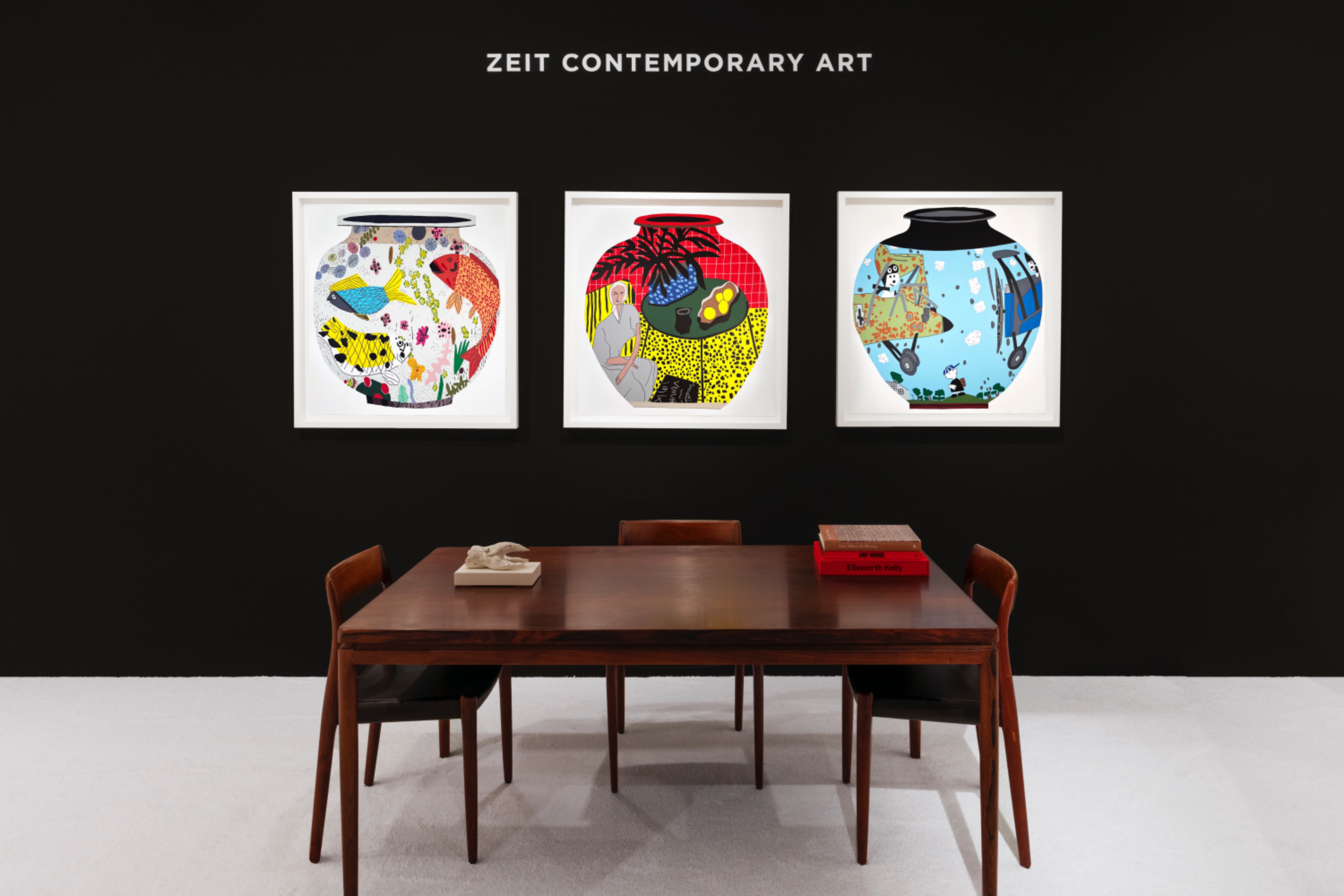 Installation view at Salon Art + Design 2023 in New York, with framed works arranged in a horizontal line on a black booth wall above a table and chairs.