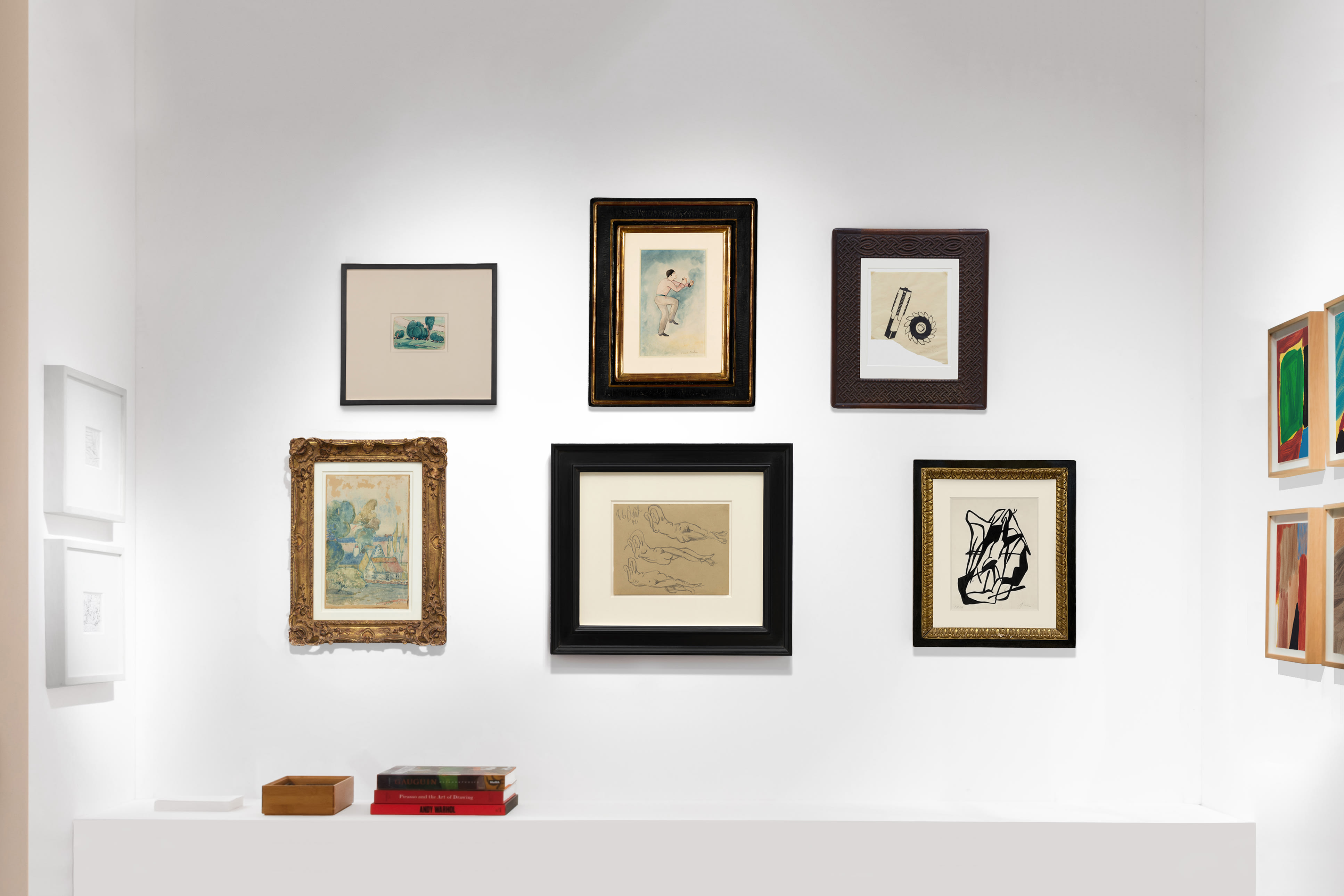 Installation view at Salon du dessin 2023 in Paris, with framed works clustered across two corner walls above a floor ledge with books.
