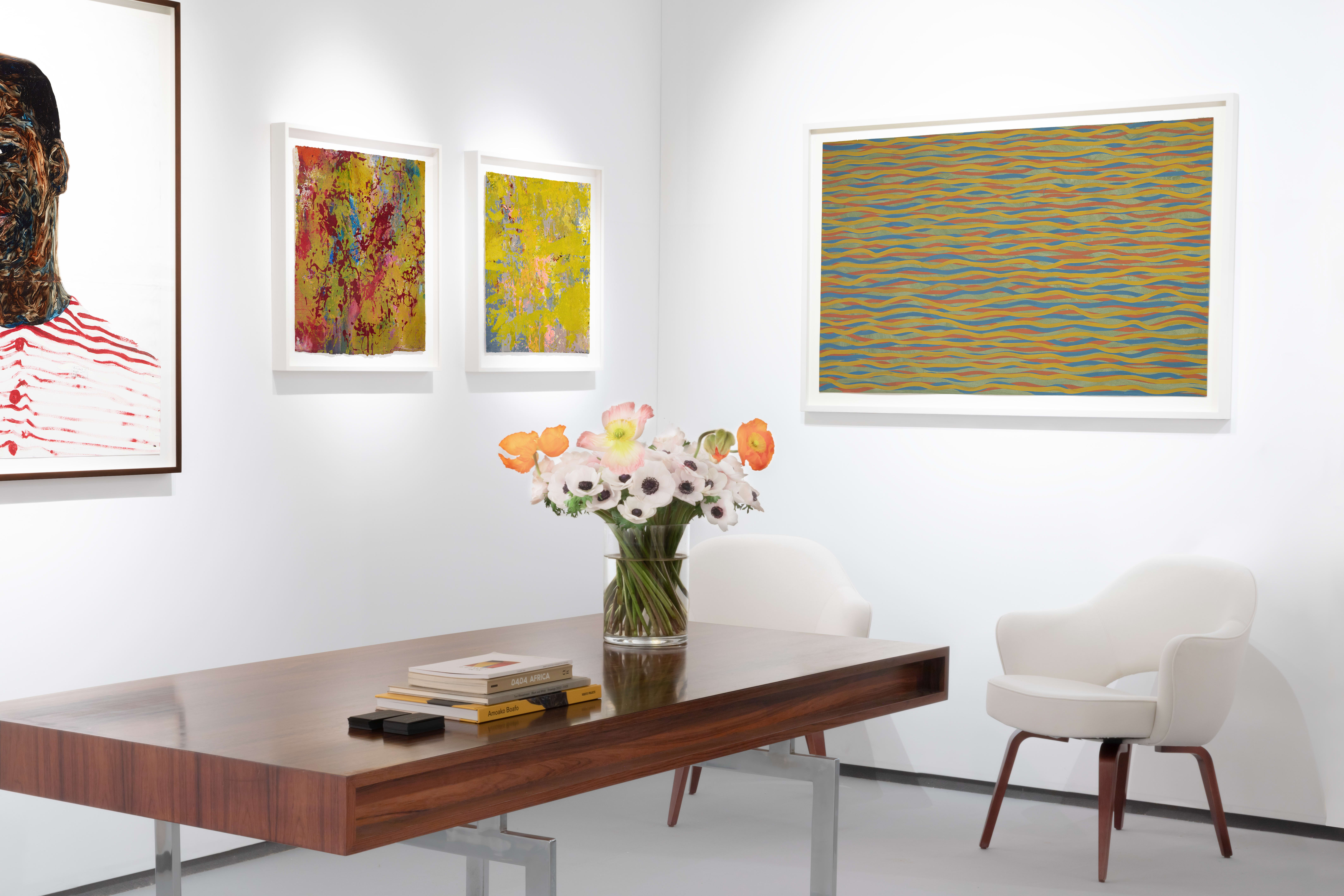 Installation view at Salon du dessin 2023 in Paris, with framed works across two corner walls surrounding a table with chairs and flowers.