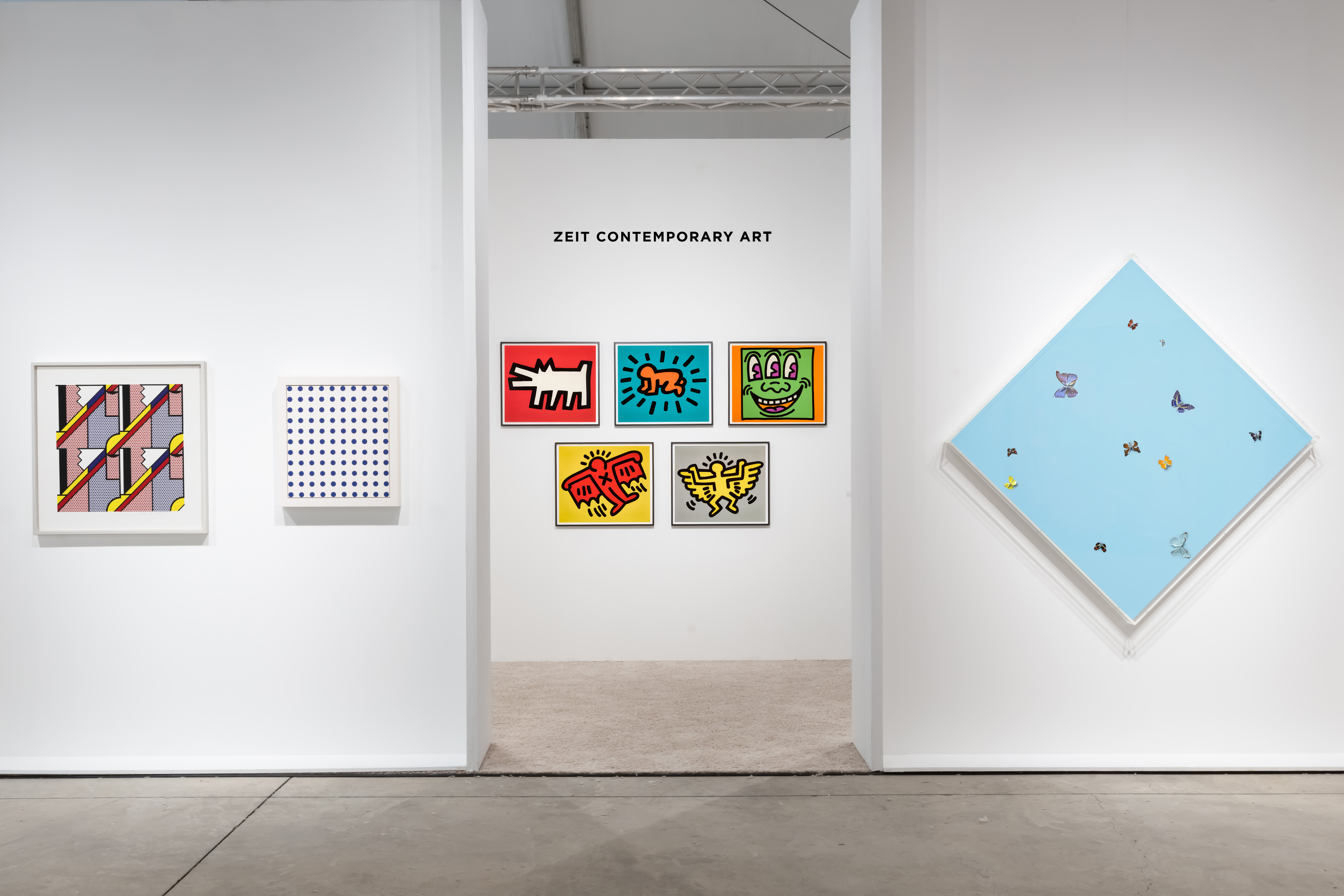 Installation view at Art Miami 2022 in Miami, with framed works across several booth walls and a clustered display on an interior wall beyond an open entryway.