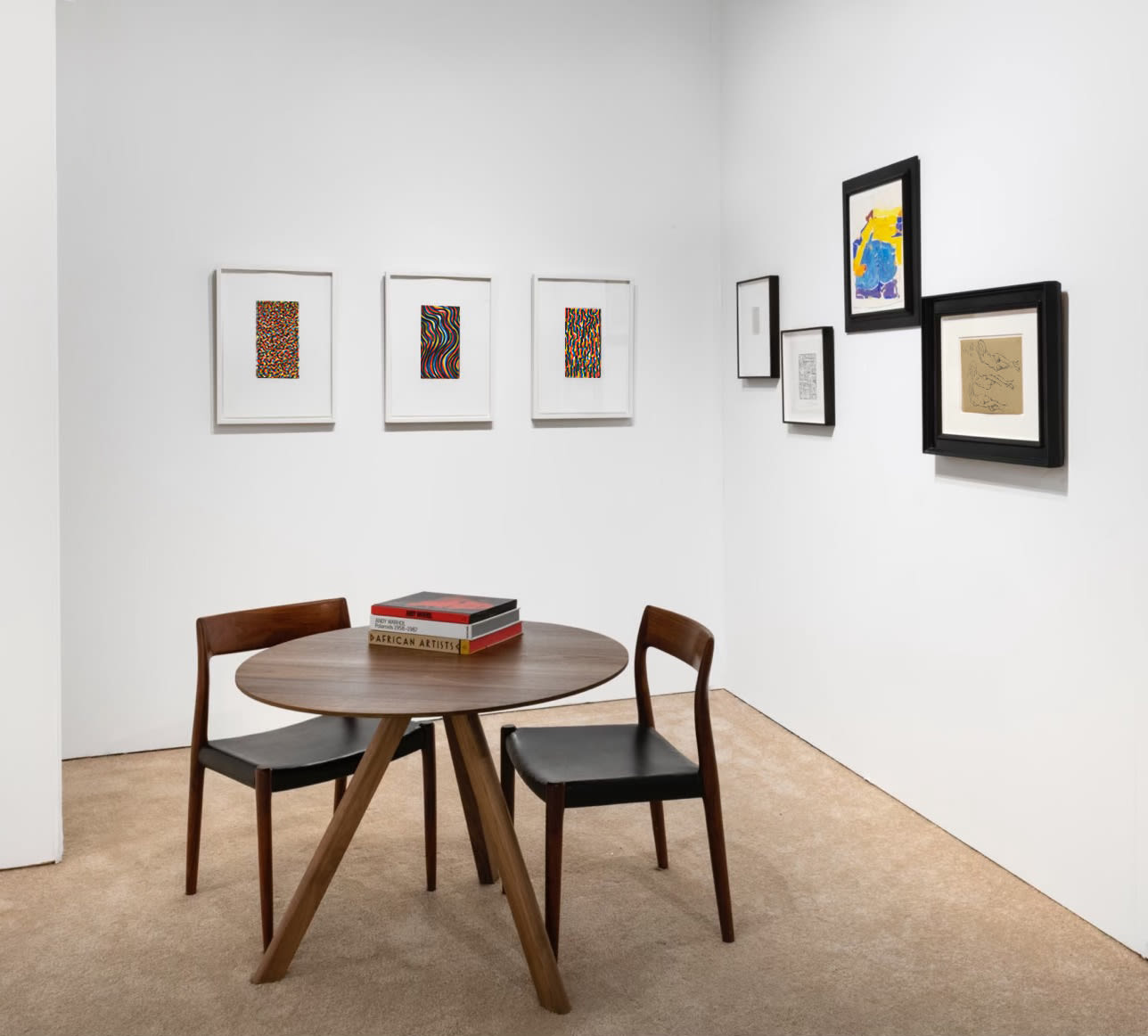 Installation view at Art Miami 2021 in Miami, with framed works arranged around a corner above a round table with books and chairs.