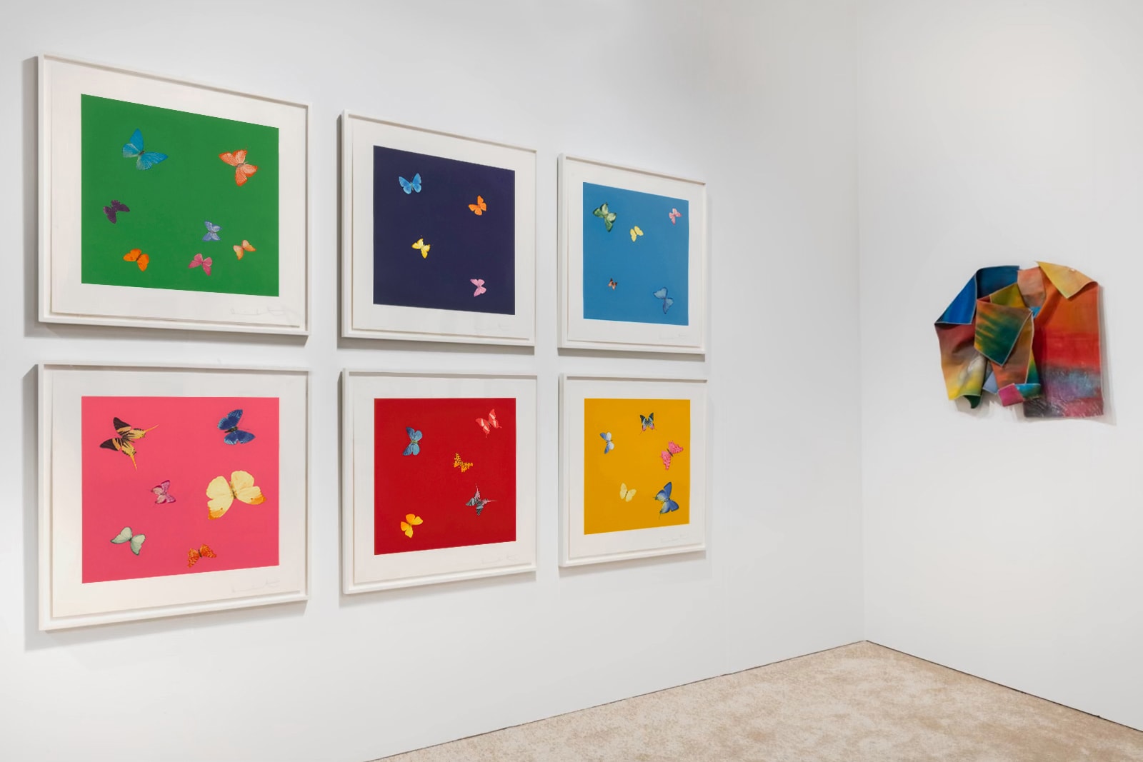 Installation view at Art Miami 2021 in Miami, with a grid of framed works on one wall and a three-dimensional work on an adjacent wall in a corner layout.