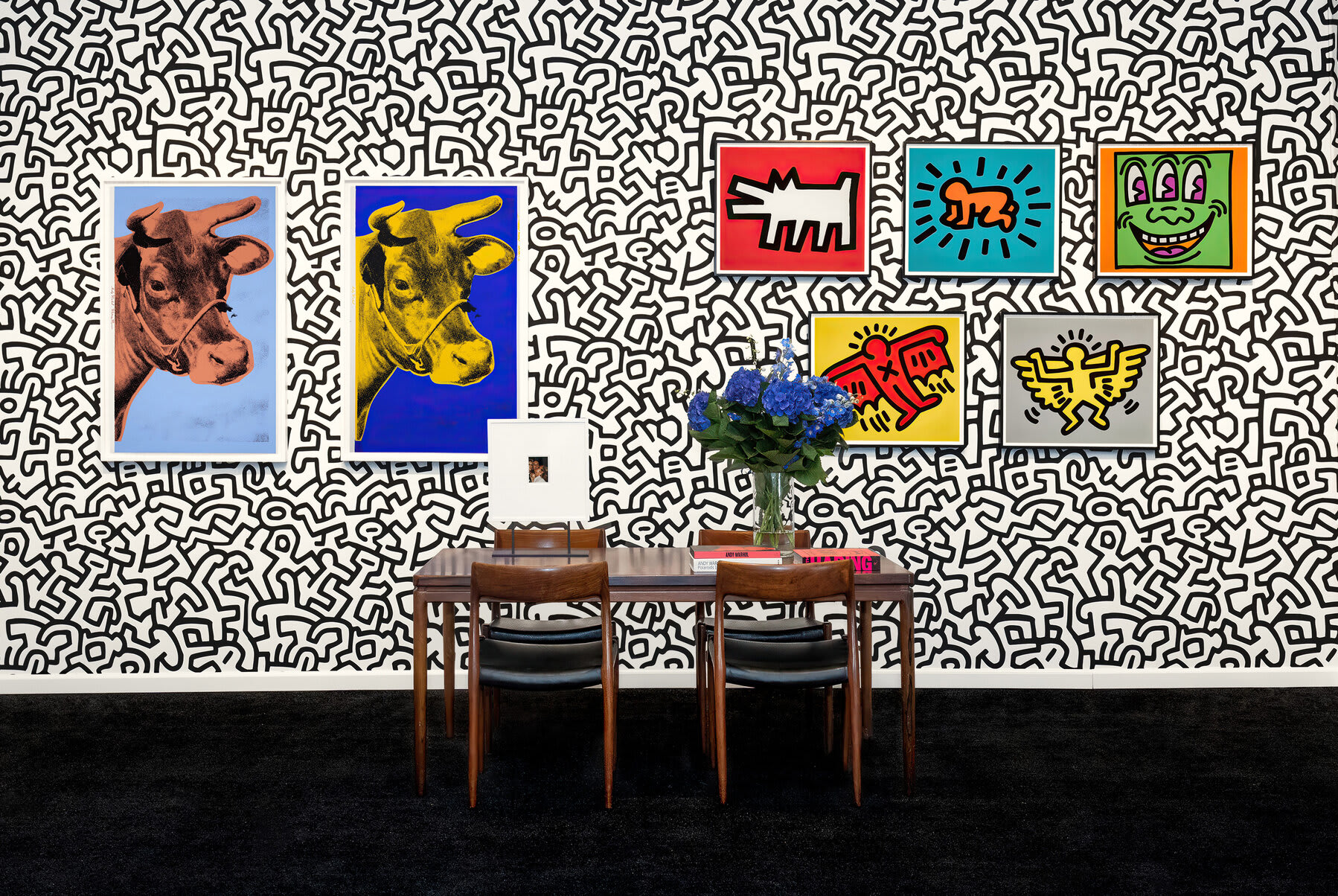 Installation view at Hamptons Fine Art Fair 2022 in Southampton, with framed works displayed on a patterned black-and-white booth wall above a seating area.