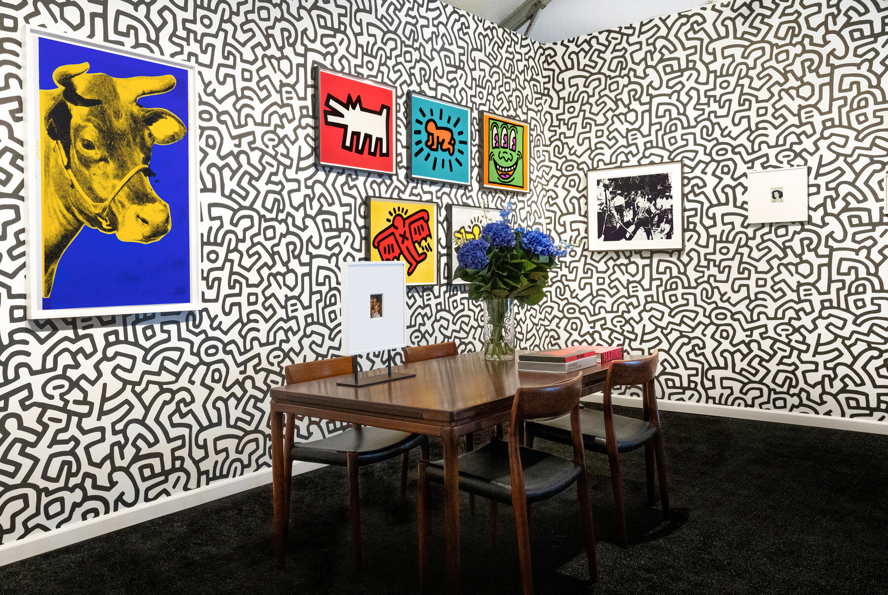 Installation view at Hamptons Fine Art Fair 2022 in Southampton, showing framed works on the booth's right wall above a table and chairs.