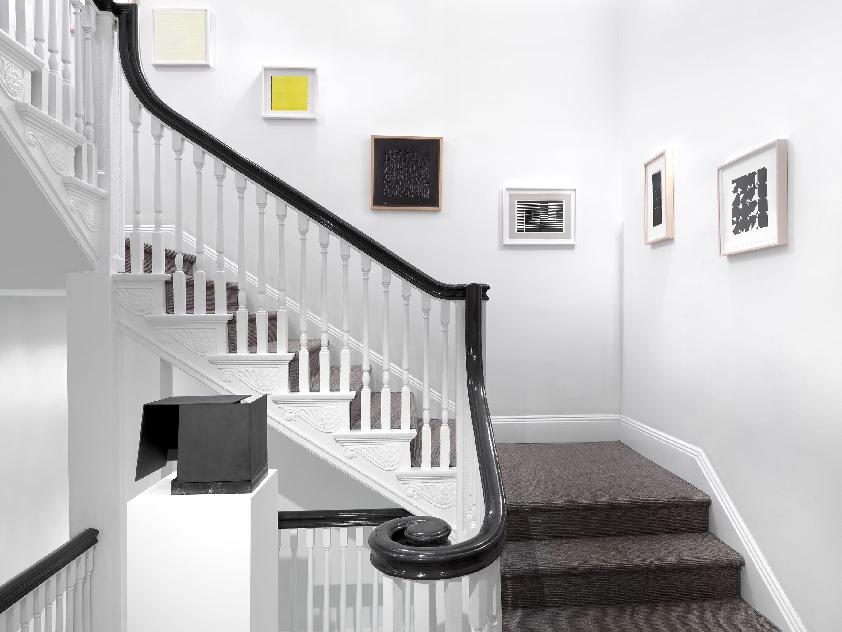 Installation view with Jorge Oteiza's Caja metafísica in the foreground and works on paper by Sol LeWitt, Willys de Castro, Anni Albers, Hélio Oiticica, Lygia Clark, and Elena Asins lining the staircase walls.