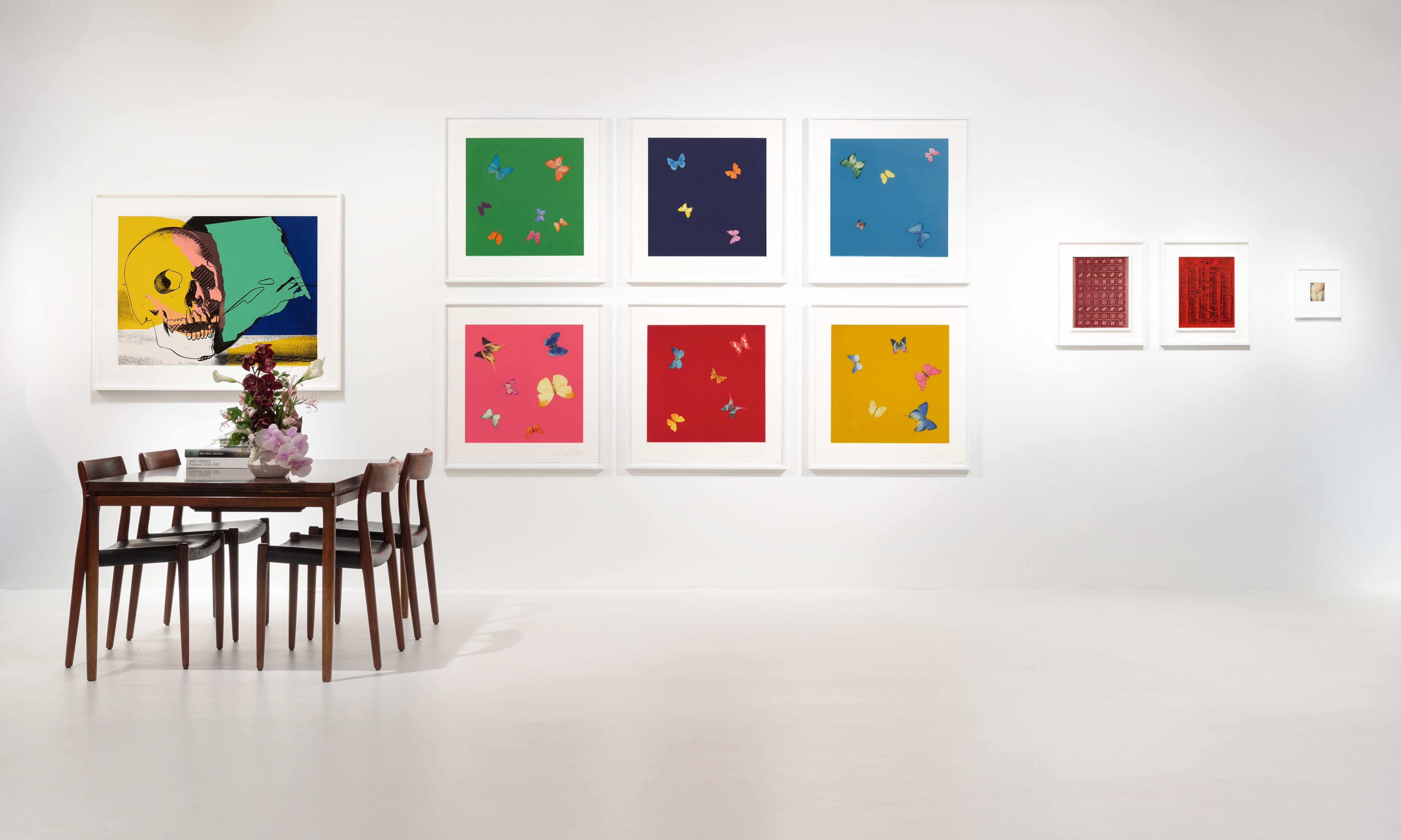 Installation view at Salon Art + Design 2024 in New York, with framed works arranged across a white booth wall above a table and chairs.