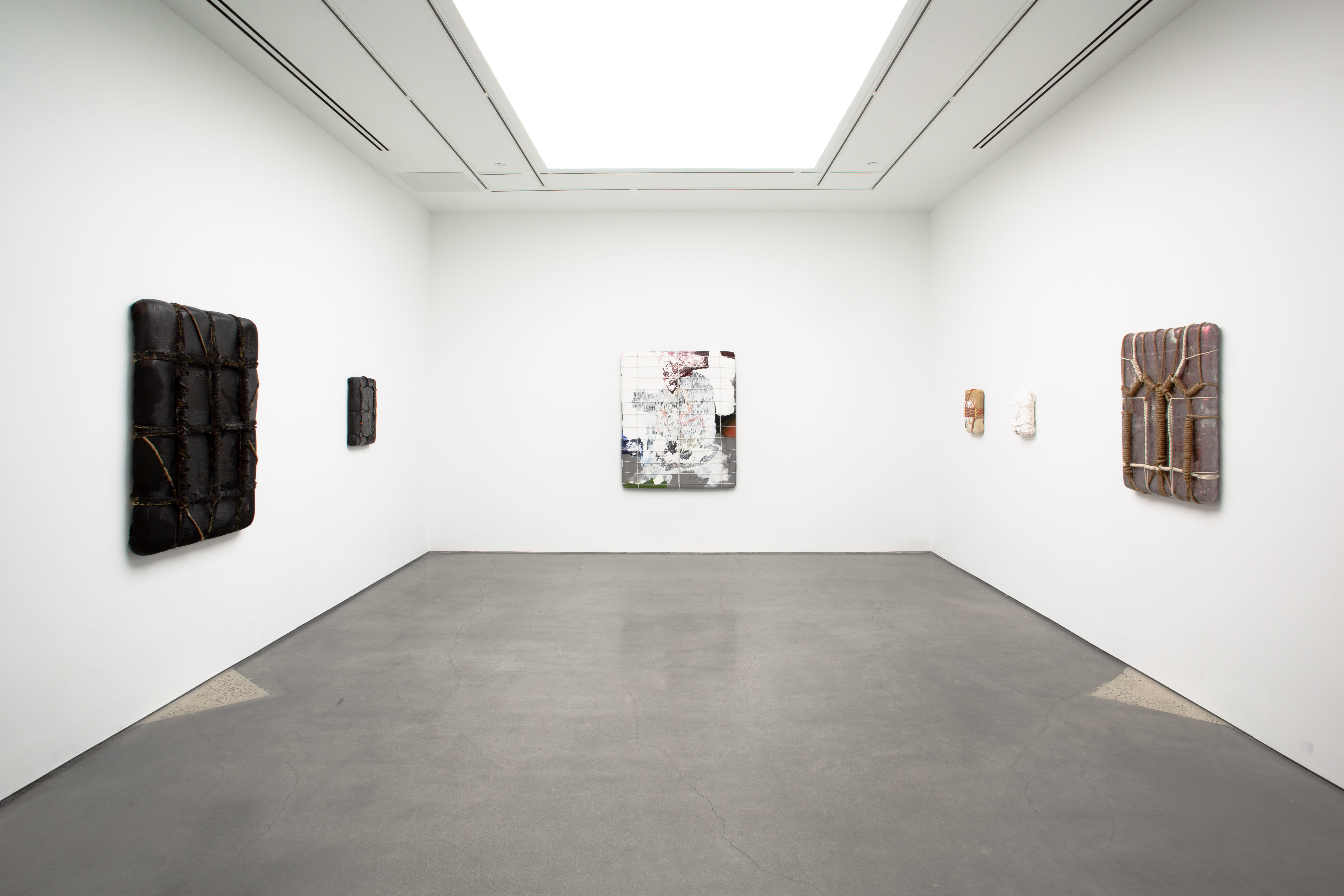 Five rectangular wall-mounted works arranged across three gallery walls, each bound with cords or ropes across its surface.