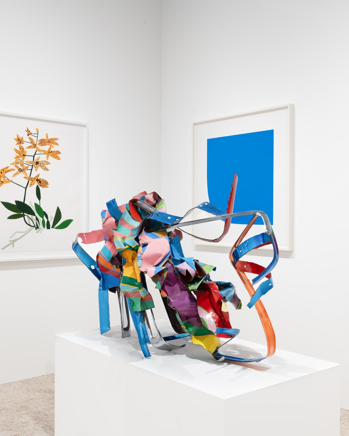 Installation view of modern and contemporary artworks with a colorful sculpture by John Chamberlain displayed among framed works by Jonas Wood and Ellsworth Kelly.