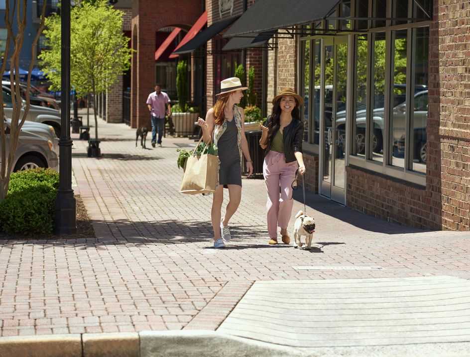 Two women walking with dog near retail shops