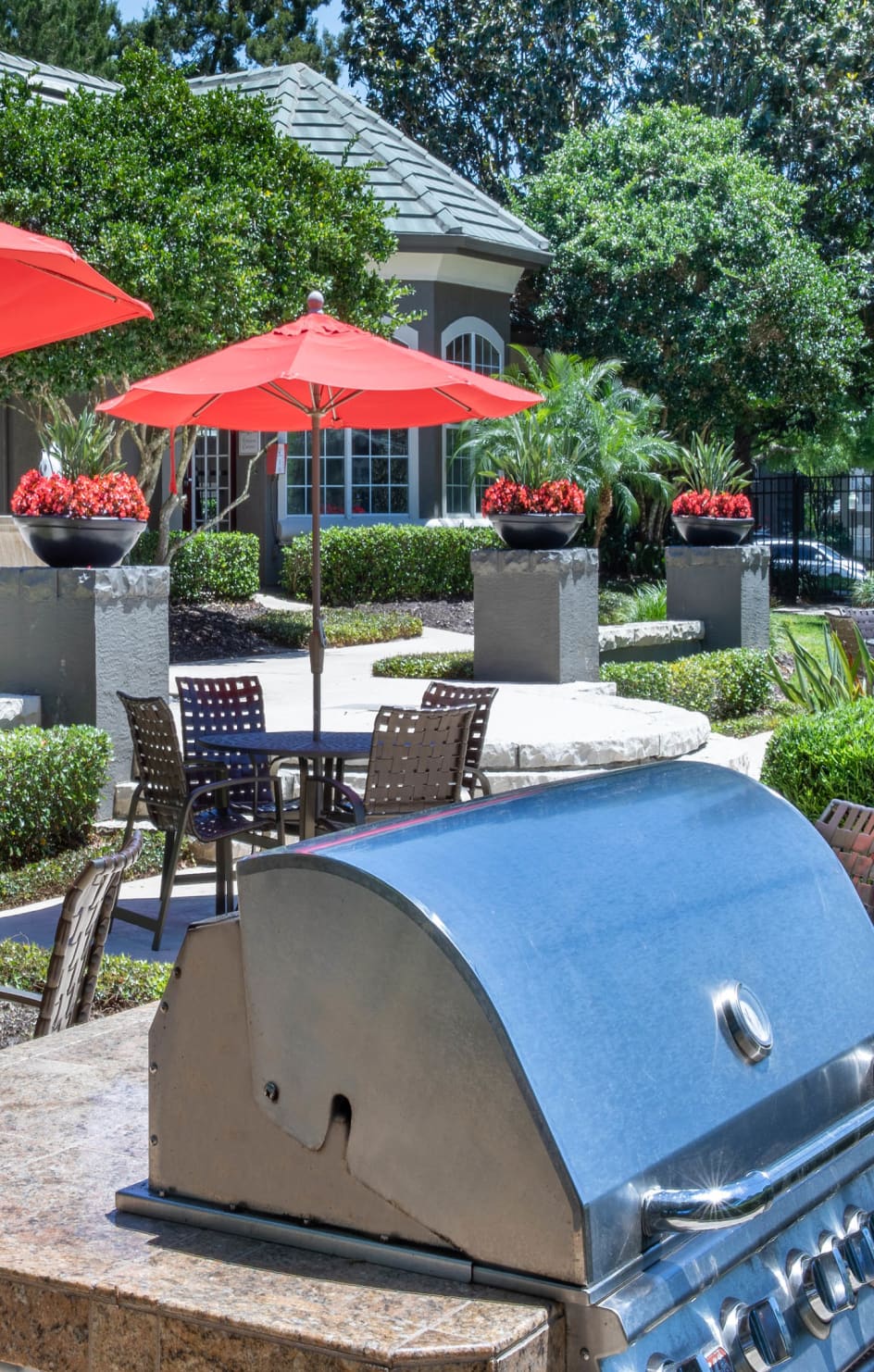 Patio tables and chairs with sun umbrellas and outdoor grilling station at MAA Heathrow luxury apartments in Orlando, FL