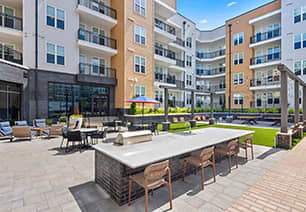 Outdoor courtyard with grilling station and table top seating next to multiple lounge areas including a grass area situated in the center of the apartment complex at MAA Nixie luxury apartments in Durham, NC