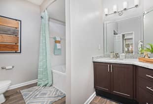 Bathroom with shower and bathtub, vanity mirror above granite counter top with dark brown cabinet and wood floors at MAA South Park luxury apartments in Charlotte, NC