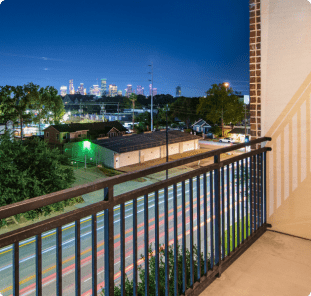 Private roadside apartment balcony with modern railings and a view of surrounding greenery and neighborhood streets at MAA Greater Heights luxury apartments in Houston, TX