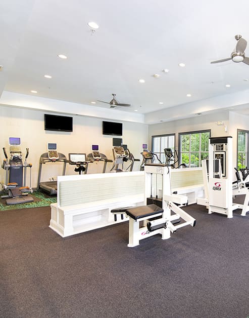 Community fitness center with weight machines, treadmills, wall mounted TVs and white bench seating at MAA Spring luxury apartments in Smyrna, GA