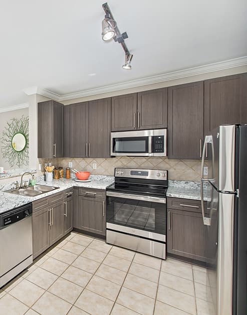 Kitchen space with brown cabinets, granite countertops and stainless steel appliances at MAA West Village luxury apartments in Smyrna, GA