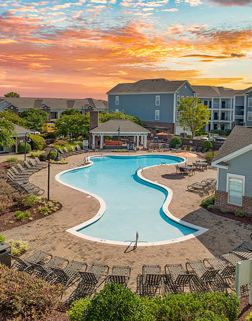 Aerial view of a resort-style pool surrounded by lounge chairs with a poolside covered patio area and lush greenery at MAA Ayrsley luxury apartments in Charlotte, NC