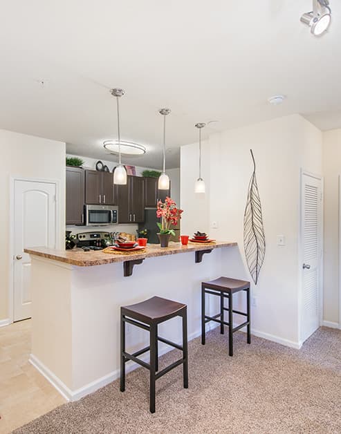 Kitchen with hanging light fixtures above bar top counter and dark brown cabinets with upgraded appliances at MAA Ayrsley luxury apartments in Charlotte, NC