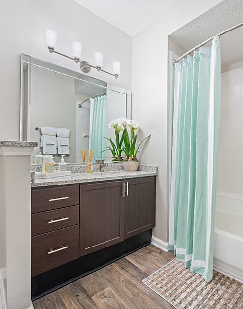 Modern bathroom with large vanity mirror, granite counter top and dark brown cabinets with wood floors at MAA South Park luxury apartments in Charlotte, NC