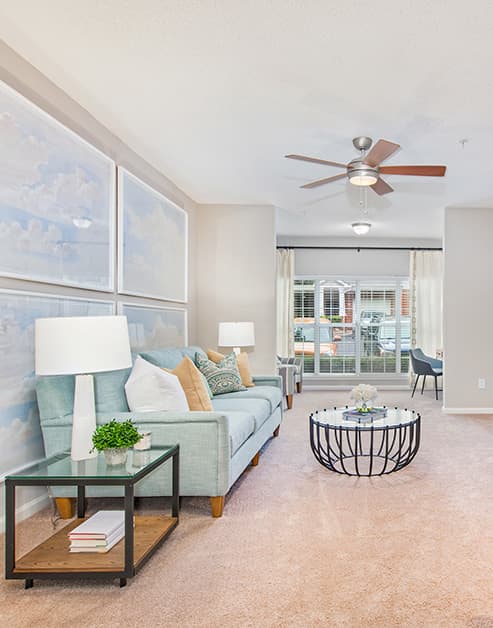 Spacious living room with ceiling fan and large wall paintings with multiple sitting areas and large picture window with curtains at MAA South Park luxury apartments in Charlotte, NC