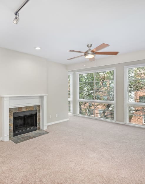 Carpeted empty living room with ceiling fan, picture windows and tiled fireplace at MAA Addison Circle luxury apartments in Addison, TX