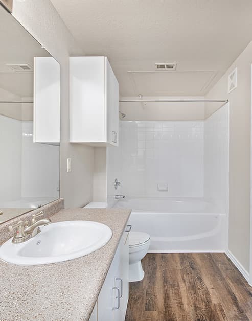 A light-toned bathroom with a light-colored countertop and white cabinets with spacious cabinets above toilet with a shower and bathtub at MAA Grand Courtyards luxury apartments in Grand Prairie, TX