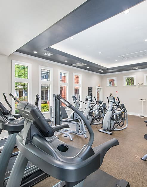A close up view of fitness center with recessed lighting and tall windows next to elliptical machines and treadmills at MAA Grand Courtyards luxury apartments in Grand Prairie, TX