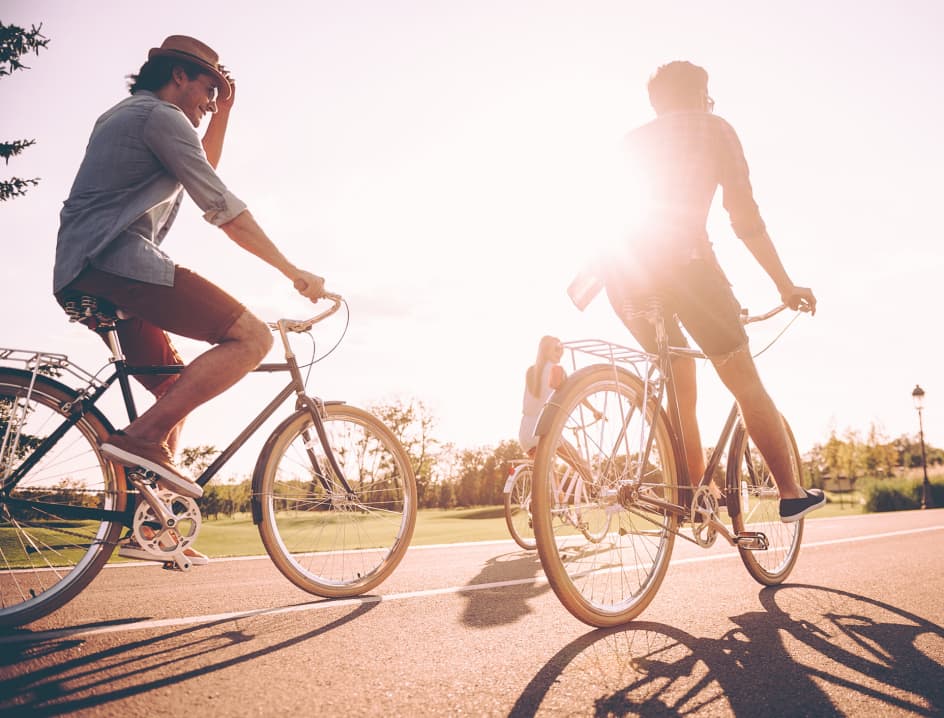 Two people ride bikes with the sun out