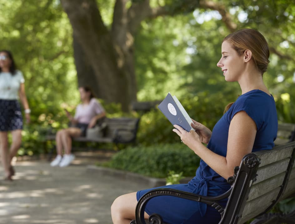Woman reading book outside with others in the background